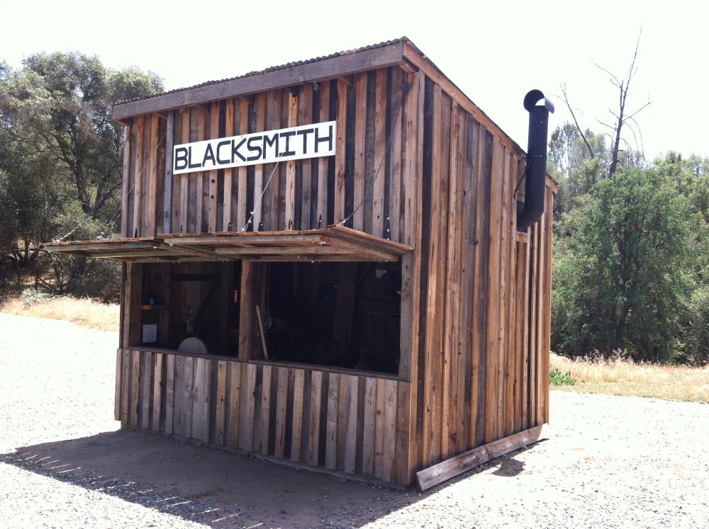 This is a photo of an old wooden building with a blacksmith sign on the front.